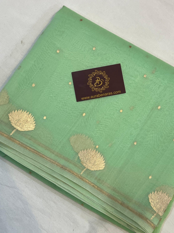 Pure Banarasi handloom Kora silk saree by Aura Benaras with small Kadhwa butis, a designer Banarasi border with Kadhwa butas, and silk blouse featuring golden zari stripes—ideal for weddings and festive wear.