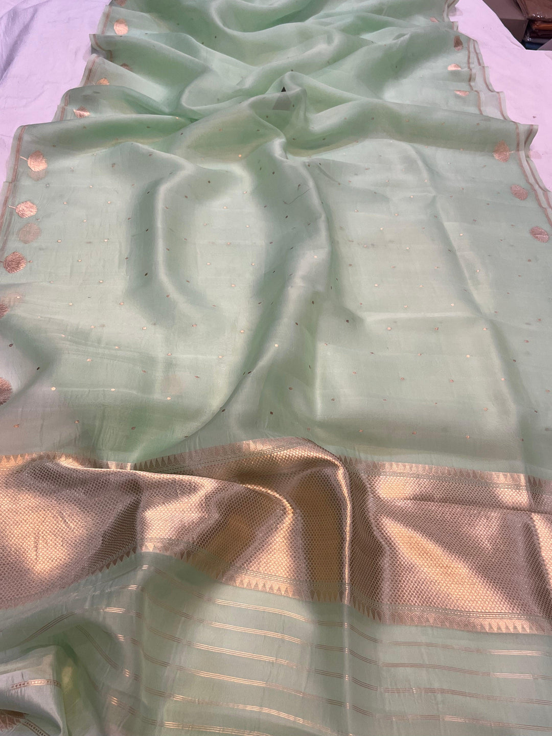 Pure Banarasi handloom Kora silk saree by Aura Benaras with small Kadhwa butis, a designer Banarasi border with Kadhwa butas, and silk blouse featuring golden zari stripes—ideal for weddings and festive wear.