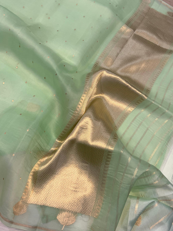 Pure Banarasi handloom Kora silk saree by Aura Benaras with small Kadhwa butis, a designer Banarasi border with Kadhwa butas, and silk blouse featuring golden zari stripes—ideal for weddings and festive wear.