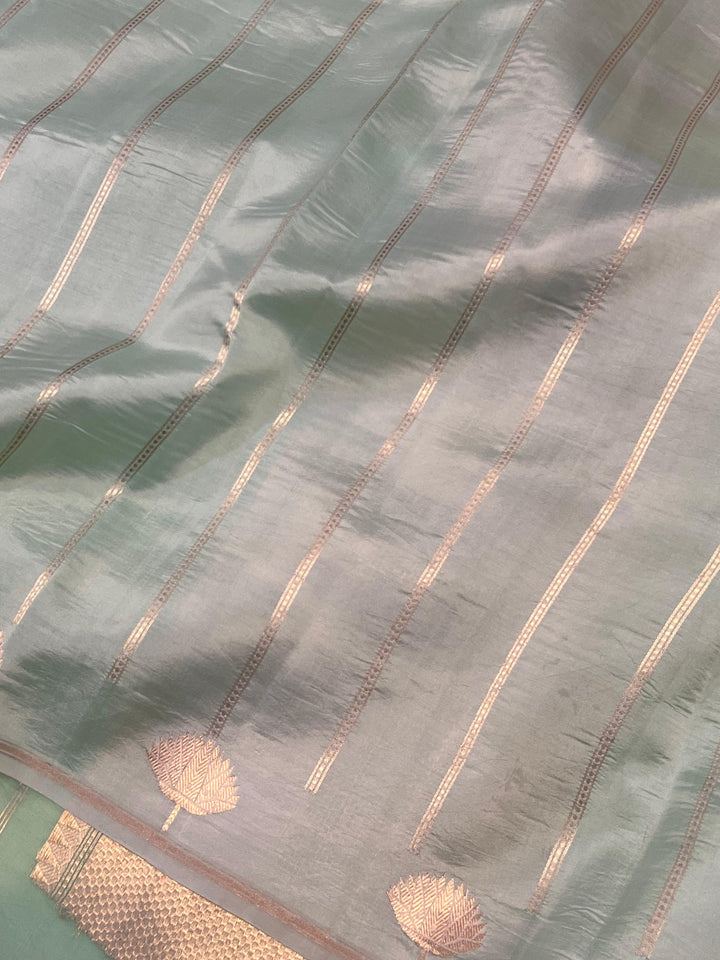 Pure Banarasi handloom Kora silk saree by Aura Benaras with small Kadhwa butis, a designer Banarasi border with Kadhwa butas, and silk blouse featuring golden zari stripes—ideal for weddings and festive wear.